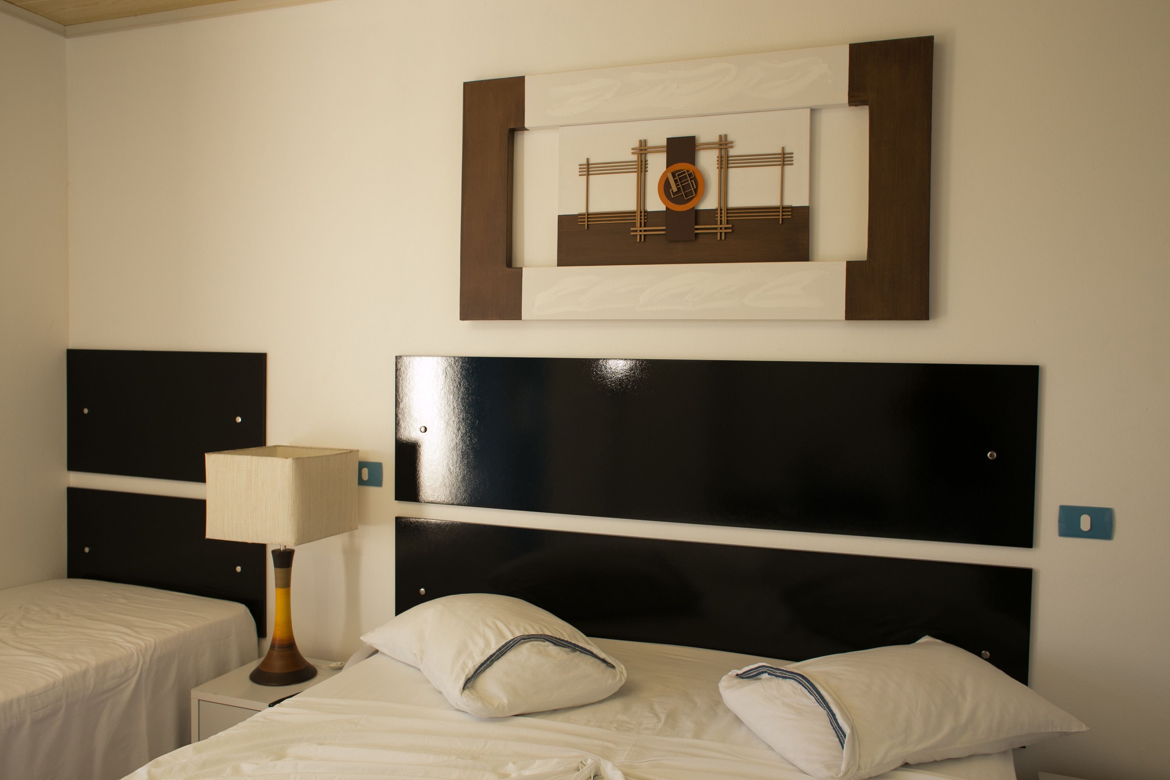 Una habitación de hotel con una cama, una mesita de noche, una lámpara y una obra de arte en la pared.