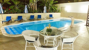 Une piscine entourée de plantes et de parasols, avec des chaises longues et une table à proximité.