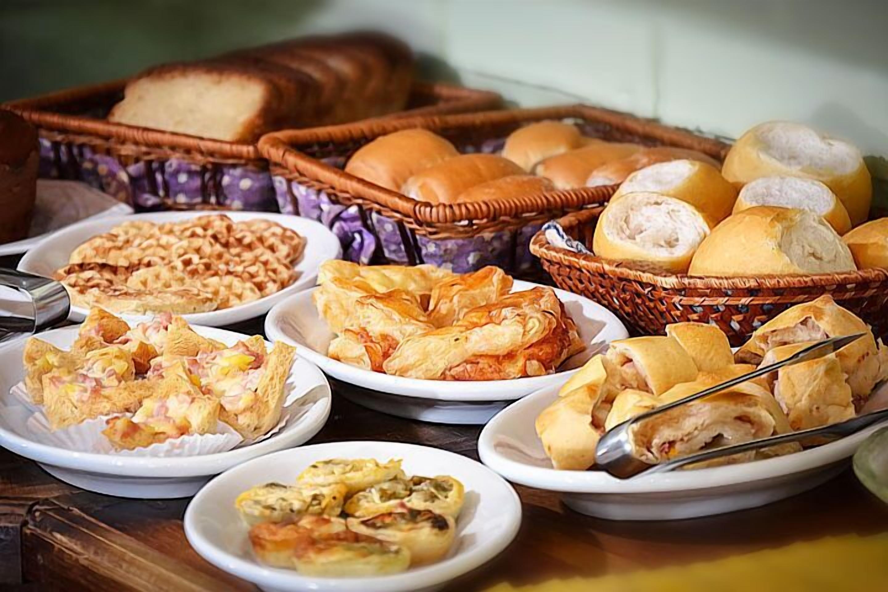 Diversos produtos de panificação, como pão, doces e pãezinhos, dispostos sobre uma mesa.