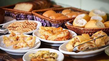 Diversos produtos de panificação, como pão, doces e pãezinhos, dispostos sobre uma mesa.