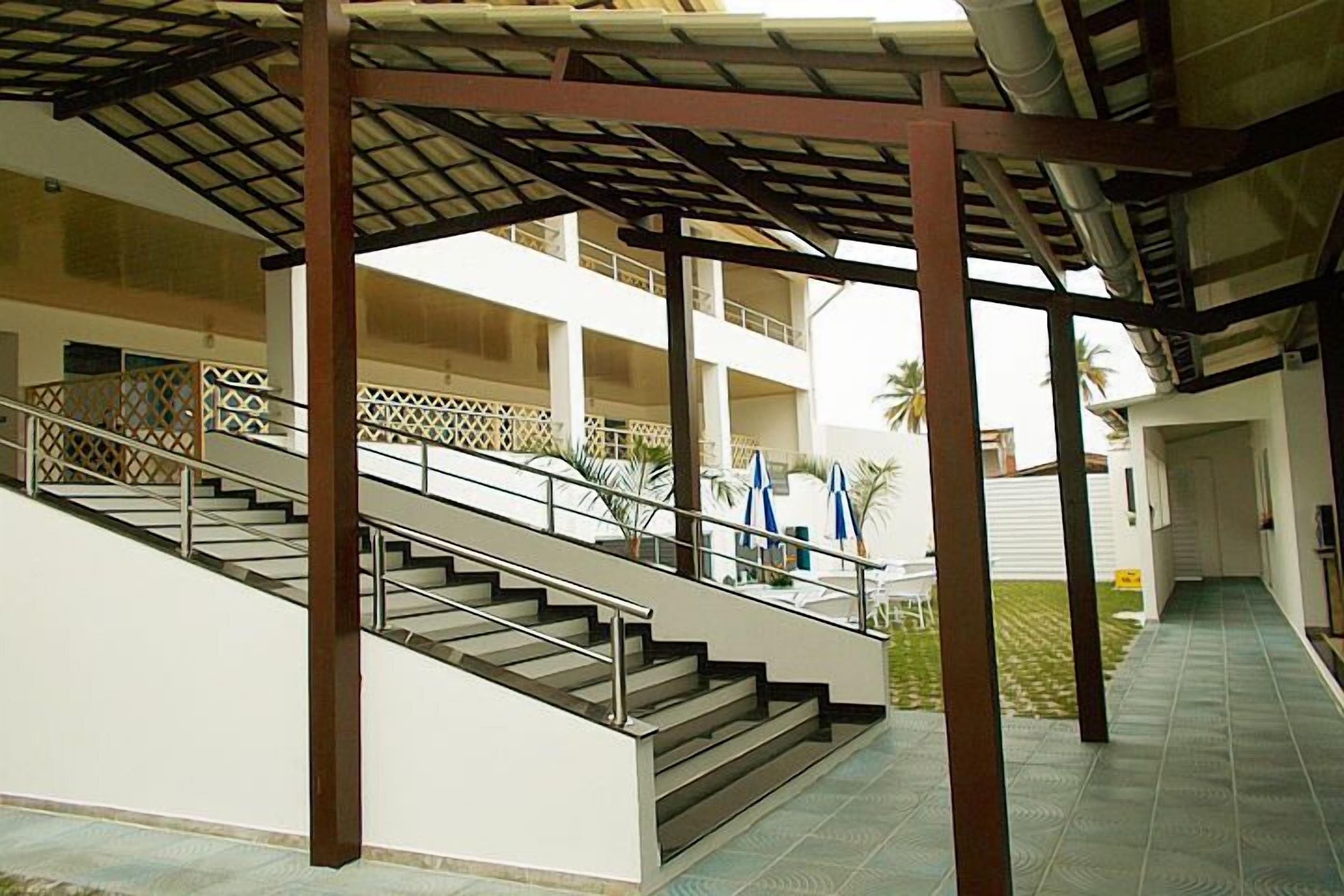 Una escalera al aire libre techada que lleva a un edificio de varios pisos, con piso de baldosas y barandilla.