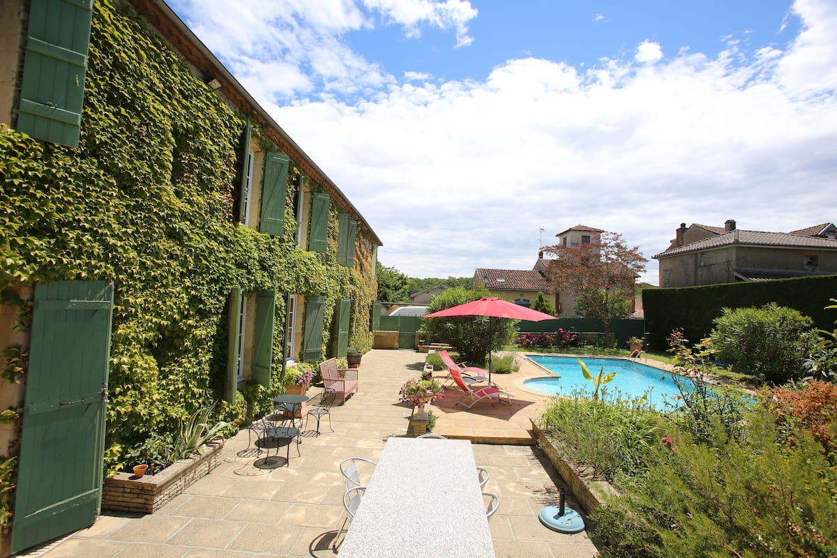 Une cour avec une piscine, un espace salon extérieur et un bâtiment recouvert de lierre.