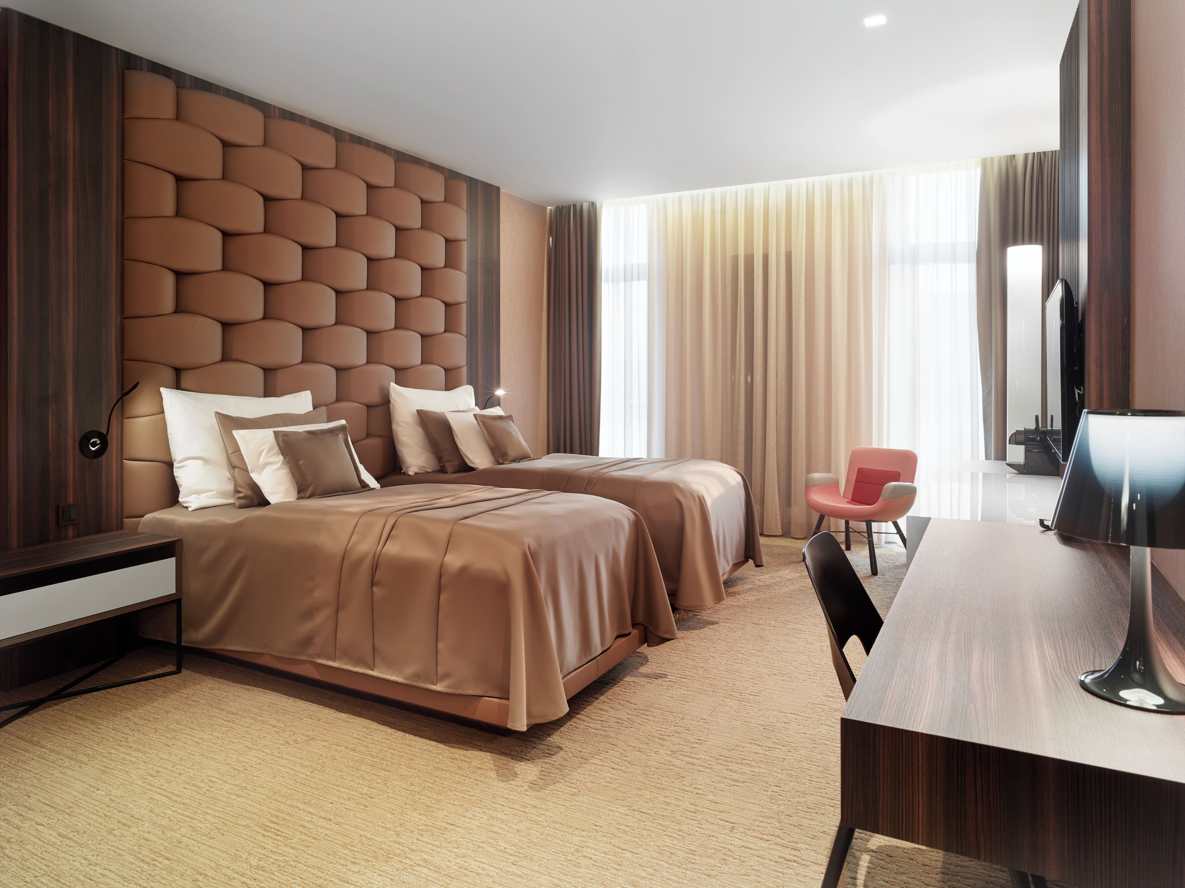A modern hotel room with two beds, a desk, a chair, and a television.
