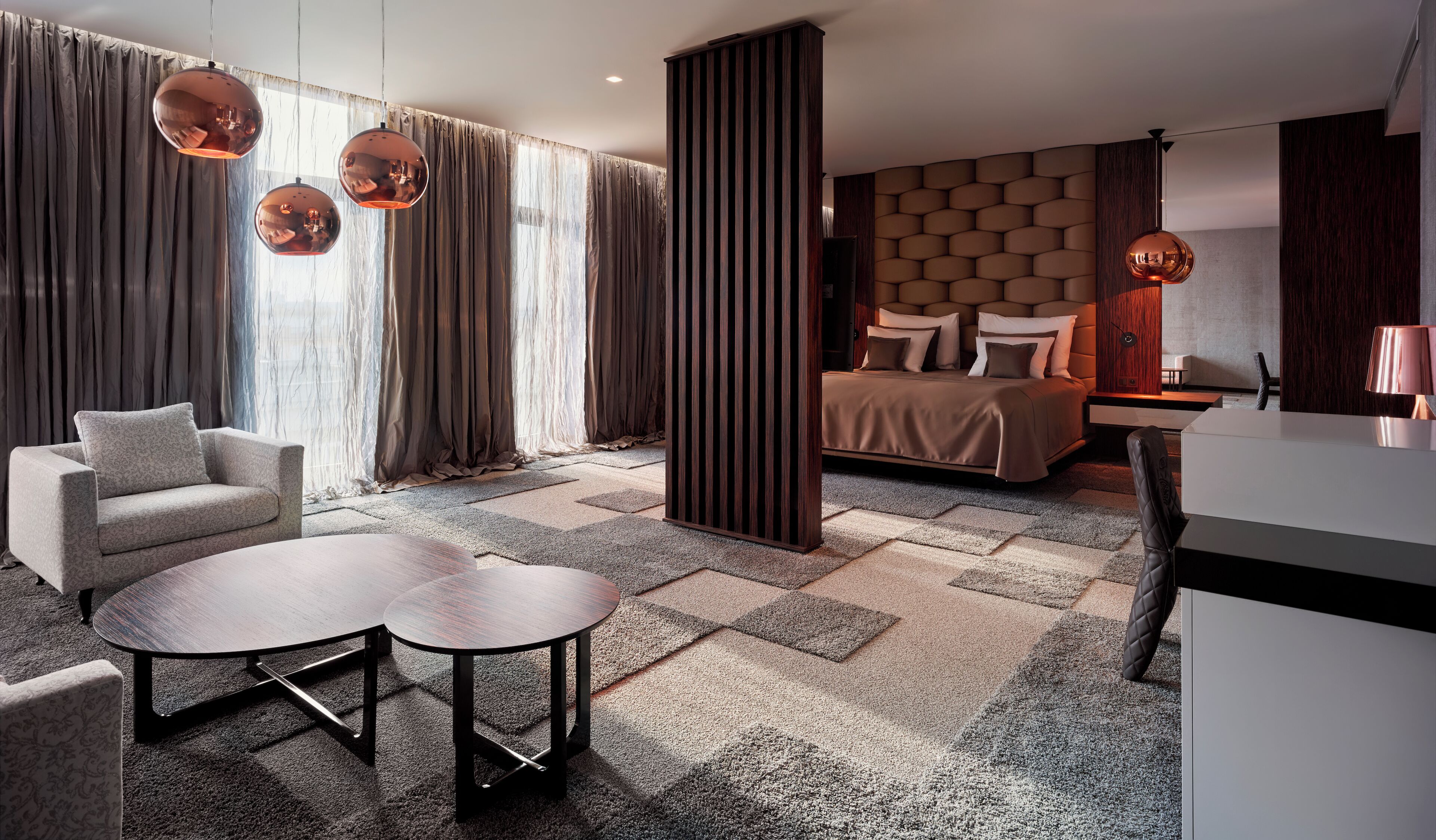 A modern hotel room with a large bed, a sofa, a coffee table, and a desk.