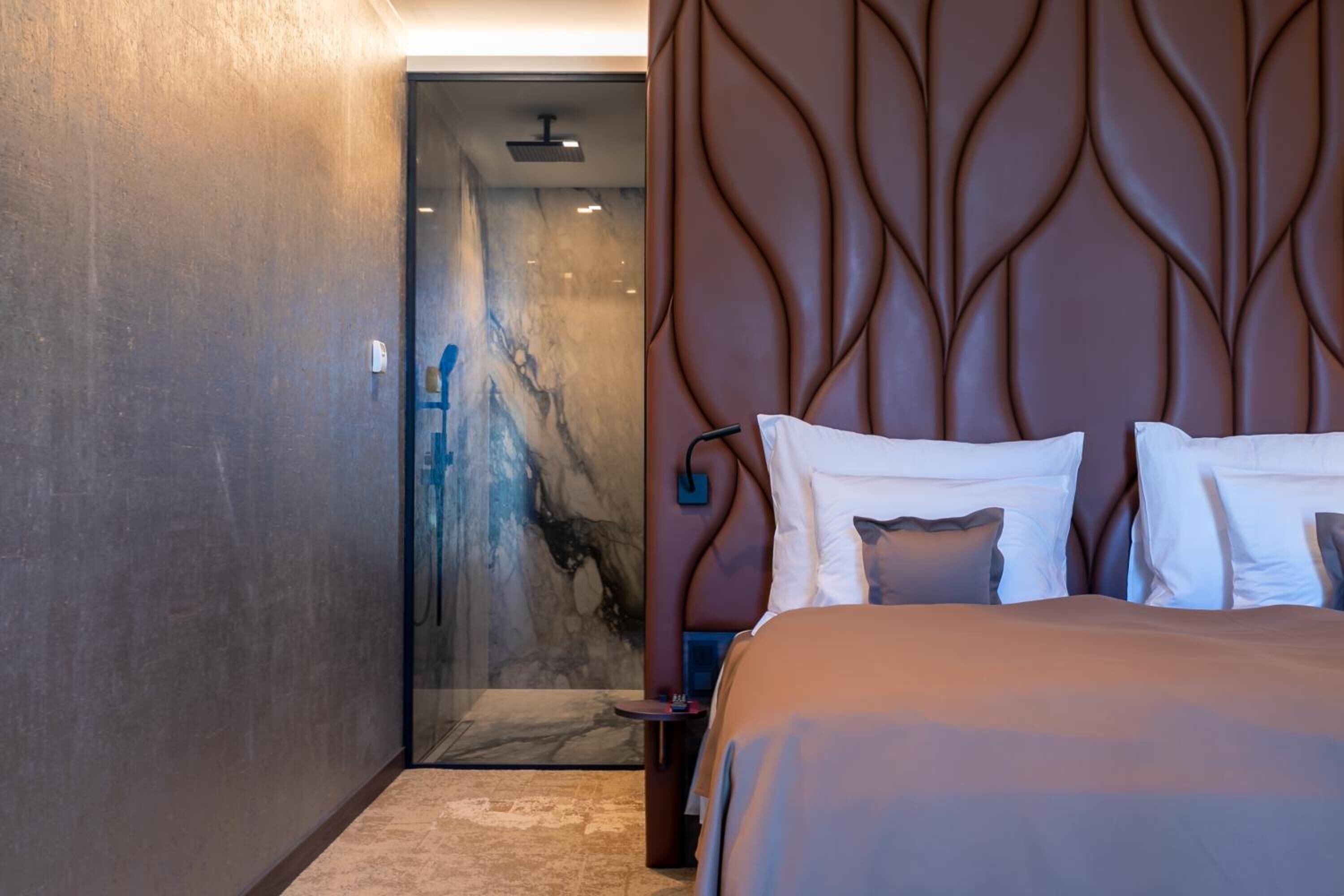 Ett modernt hotellrum med en säng, en duschkabin med glasväggar och en vägg beklädd med marmor.