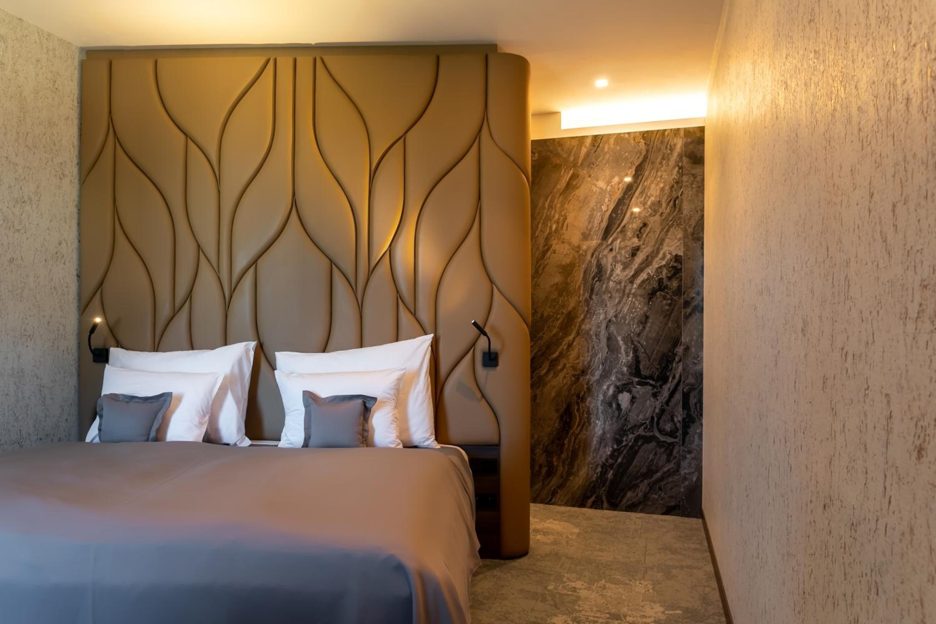 Una habitación de hotel moderna con una cama grande, una pared decorativa de mármol y un cabecero con una textura original.