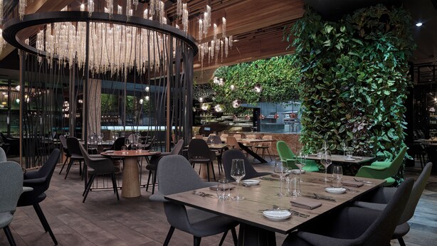 A modern restaurant interior with wooden flooring, black and grey chairs, a central chandelier, and a green vertical garden wall. - Theatre Hotel (Olomouc)