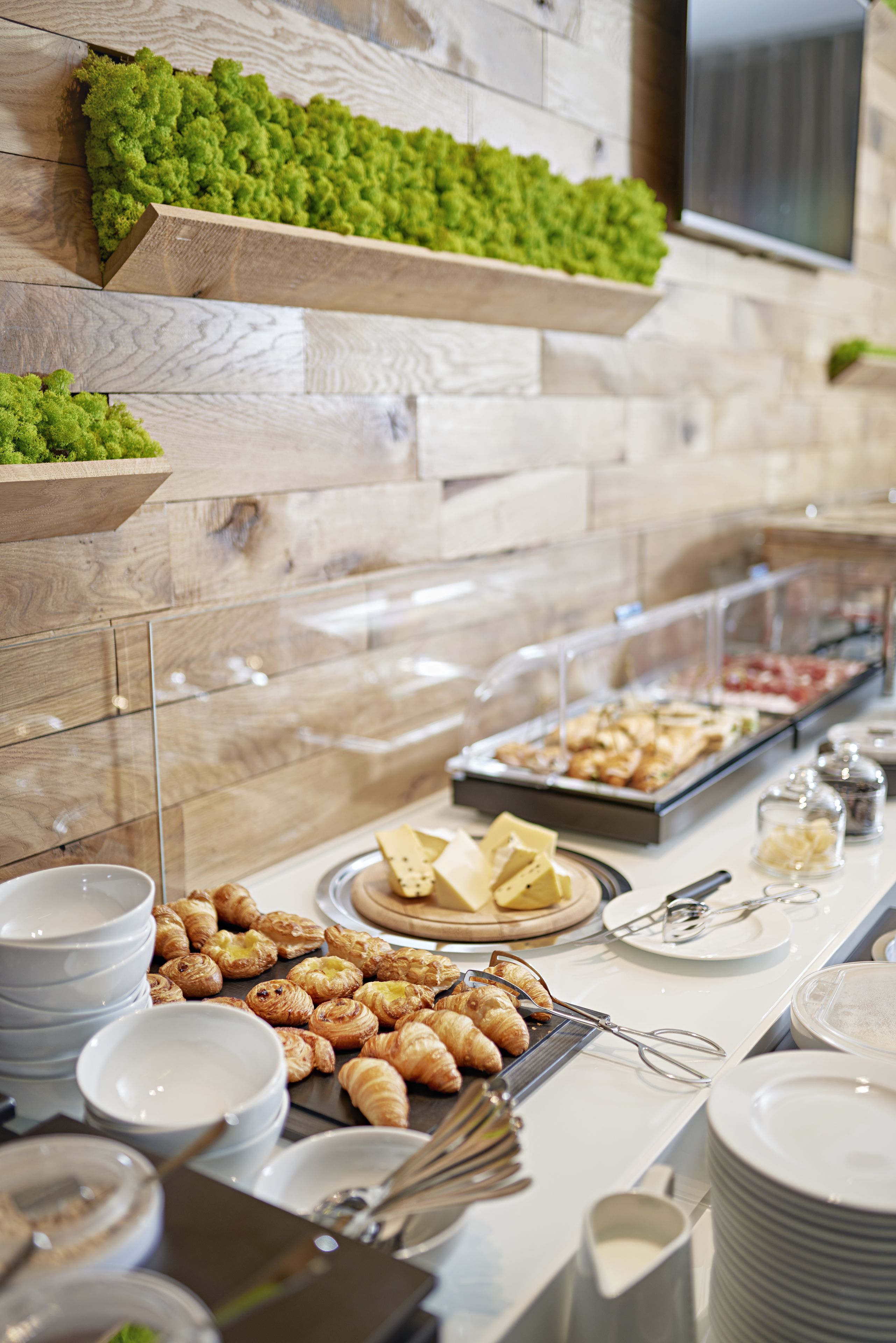 A buffet with various food items, including pastries and cheeses, arranged on a table with a wooden backdrop and a mounted television.