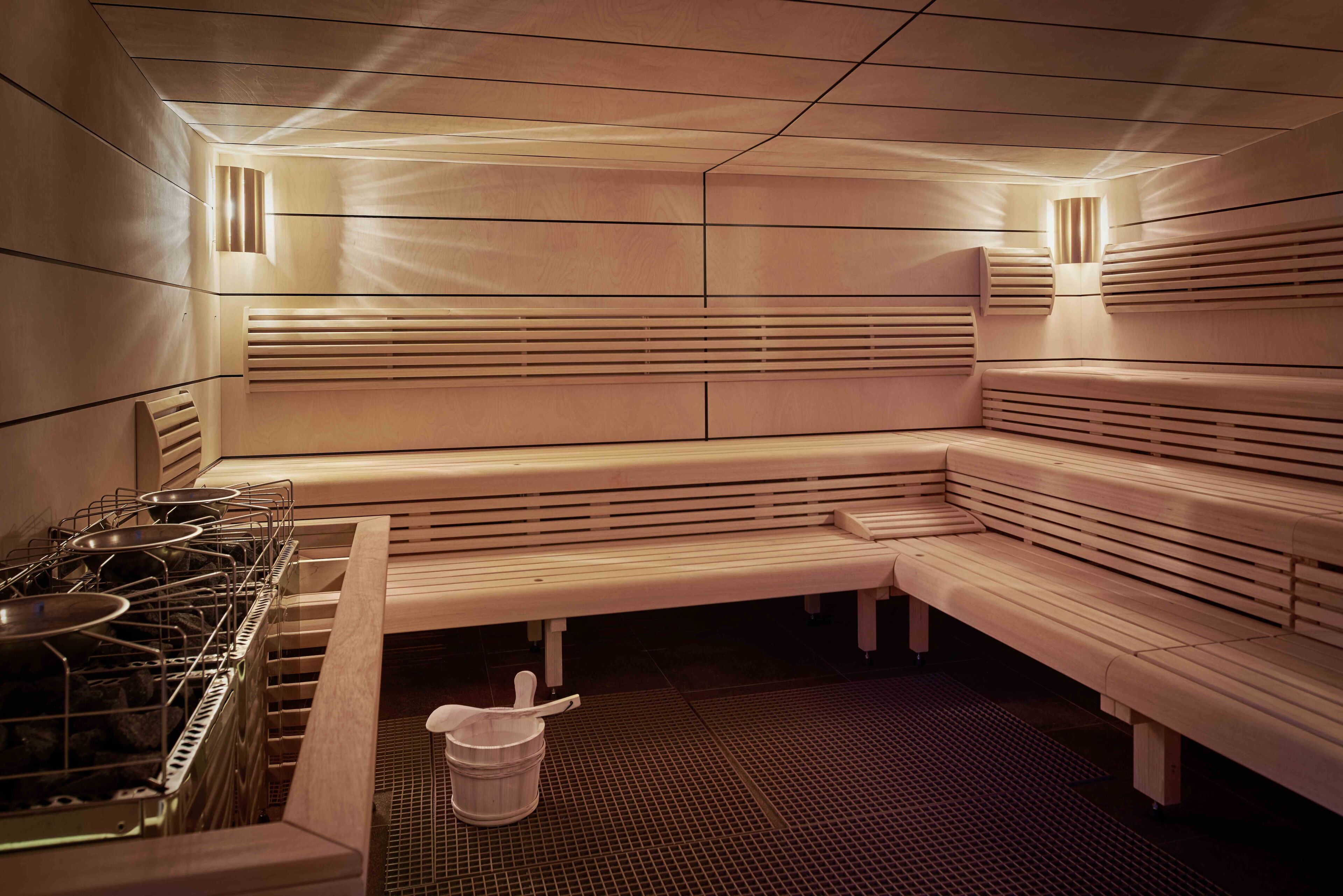 A sauna with benches, a stove, and a bucket.