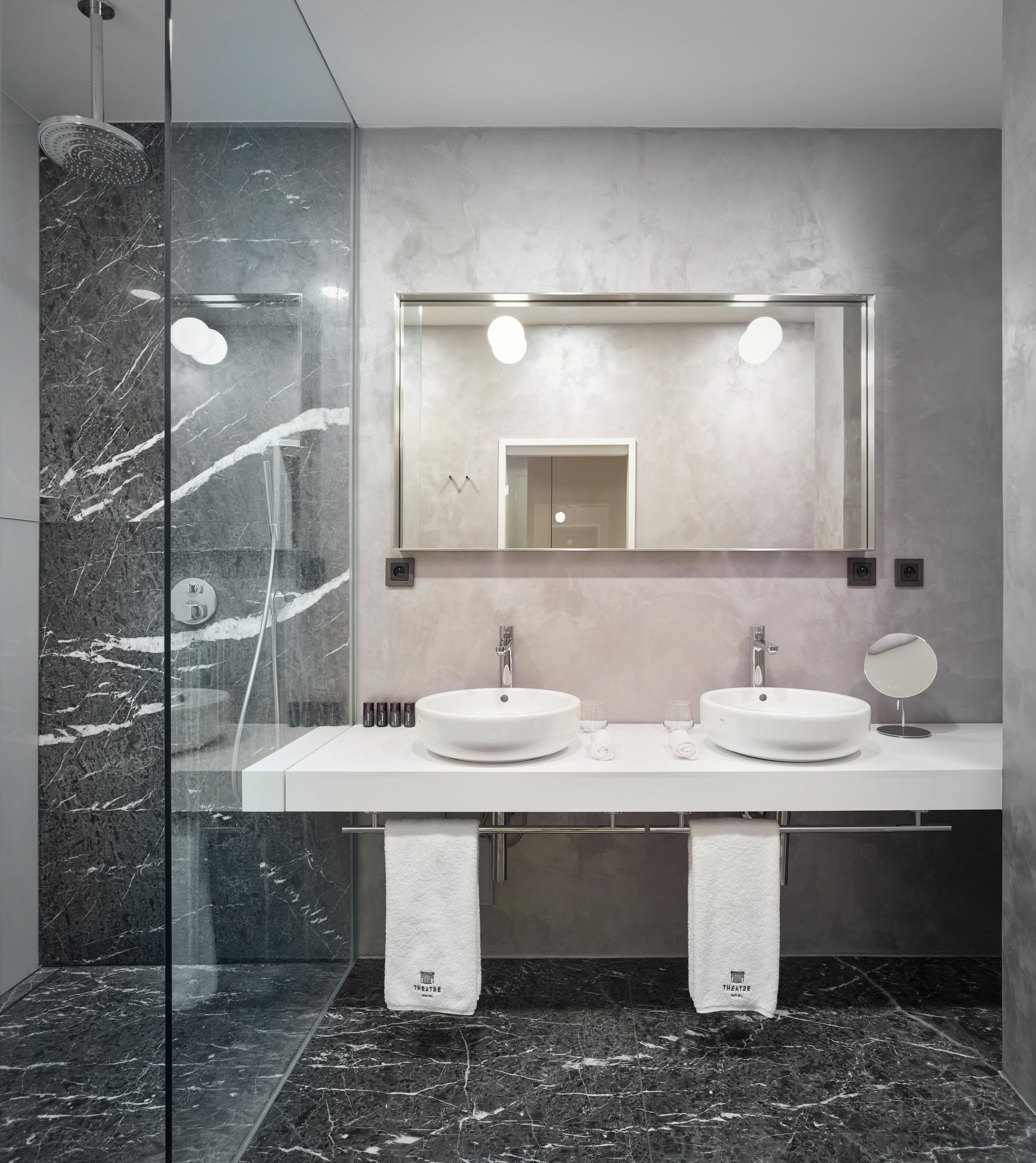 Une salle de bain moderne avec une douche en verre, deux lavabos, un grand miroir et un sol en marbre.