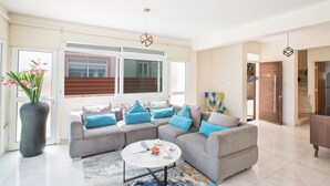 A modern living room with a sectional sofa, a coffee table, and a large window. - Shaye Frontline Villa (Paralimni)