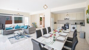A modern living room with a dining area, kitchen, and laundry facilities. - Shaye Frontline Villa (Paralimni)