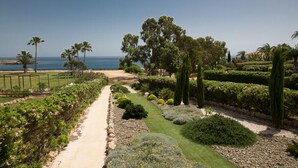 A landscaped garden with a pathway, various plants, and a view of the ocean. - Shaye Frontline Villa (Paralimni)