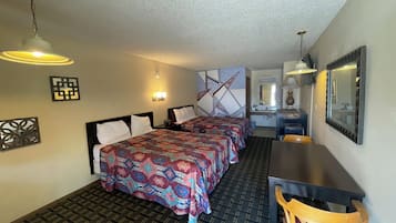A hotel room with two beds, a desk, and a chair. There is a mirror, a wall clock, and a decorative wall piece.