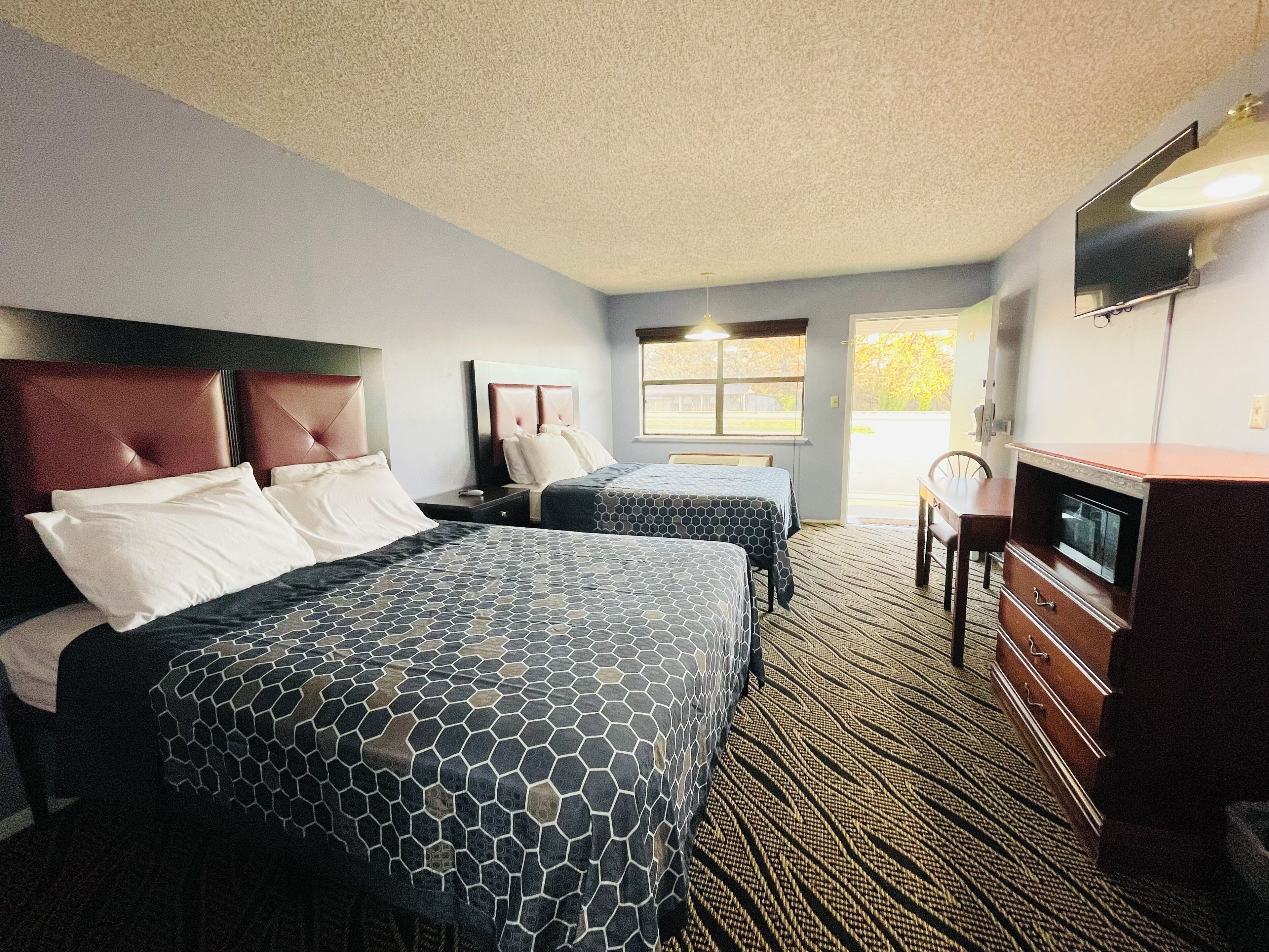 A hotel room with two beds, a TV, a dresser, and a window.