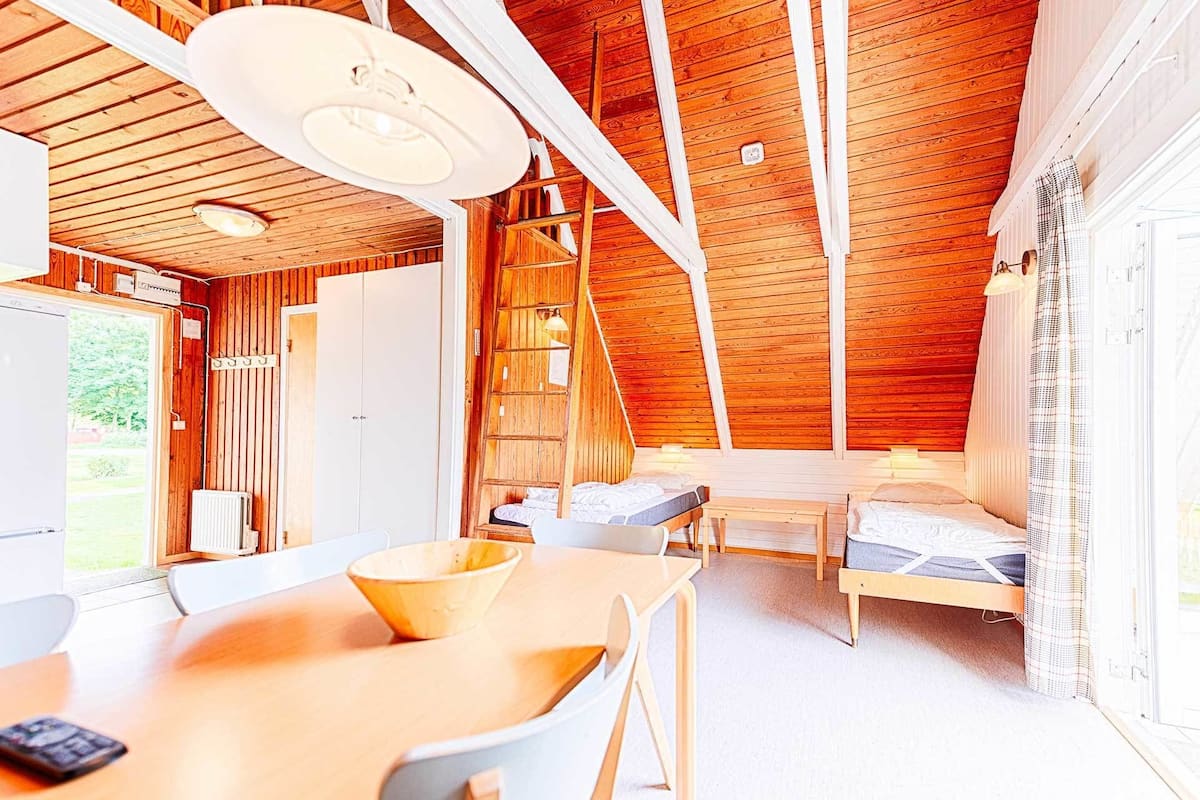 A cozy cabin with a wooden interior, a dining area with a table and chairs, and two beds.