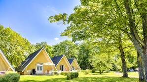 Une rangée de cabanes jaunes, avec une pelouse verdoyante et des arbres en arrière-plan.
