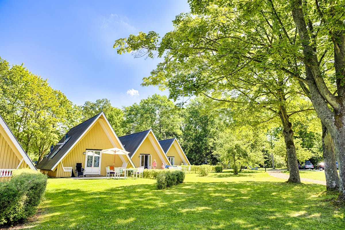 A row of yellow cabins with a grassy lawn and trees in the background.