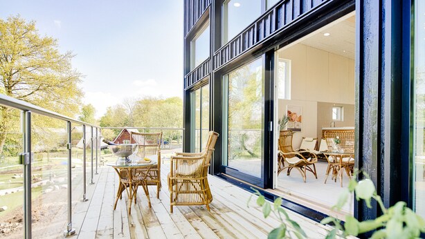 Une terrasse en bois, meublée de mobilier en osier, et une porte vitrée donnant sur un espace intérieur.