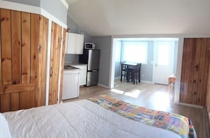 Un dormitorio con cama, armario de madera, kitchenette y zona de comedor con mesa y sillas.