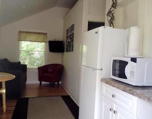 Cocina compacta con microondas, refrigerador y un pequeño comedor con mesa y una silla roja.