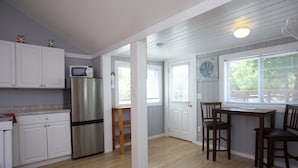 A kitchen with white cabinets, a stainless steel refrigerator, a wooden table, and a window with blinds. - Drakes Island Resort (Wells)