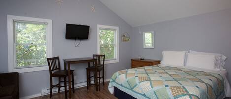 A bedroom with a bed, two windows, a desk with a chair, a TV, and a nightstand.