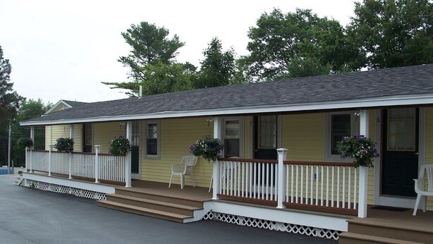 A motel with a two-story structure, a porch with white railings, and two chairs outside. - Drakes Island Resort (Wells)