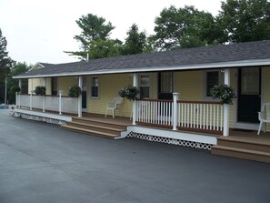 A motel with a two-story structure, a porch with white railings, and two chairs outside. - Drakes Island Resort (Wells)