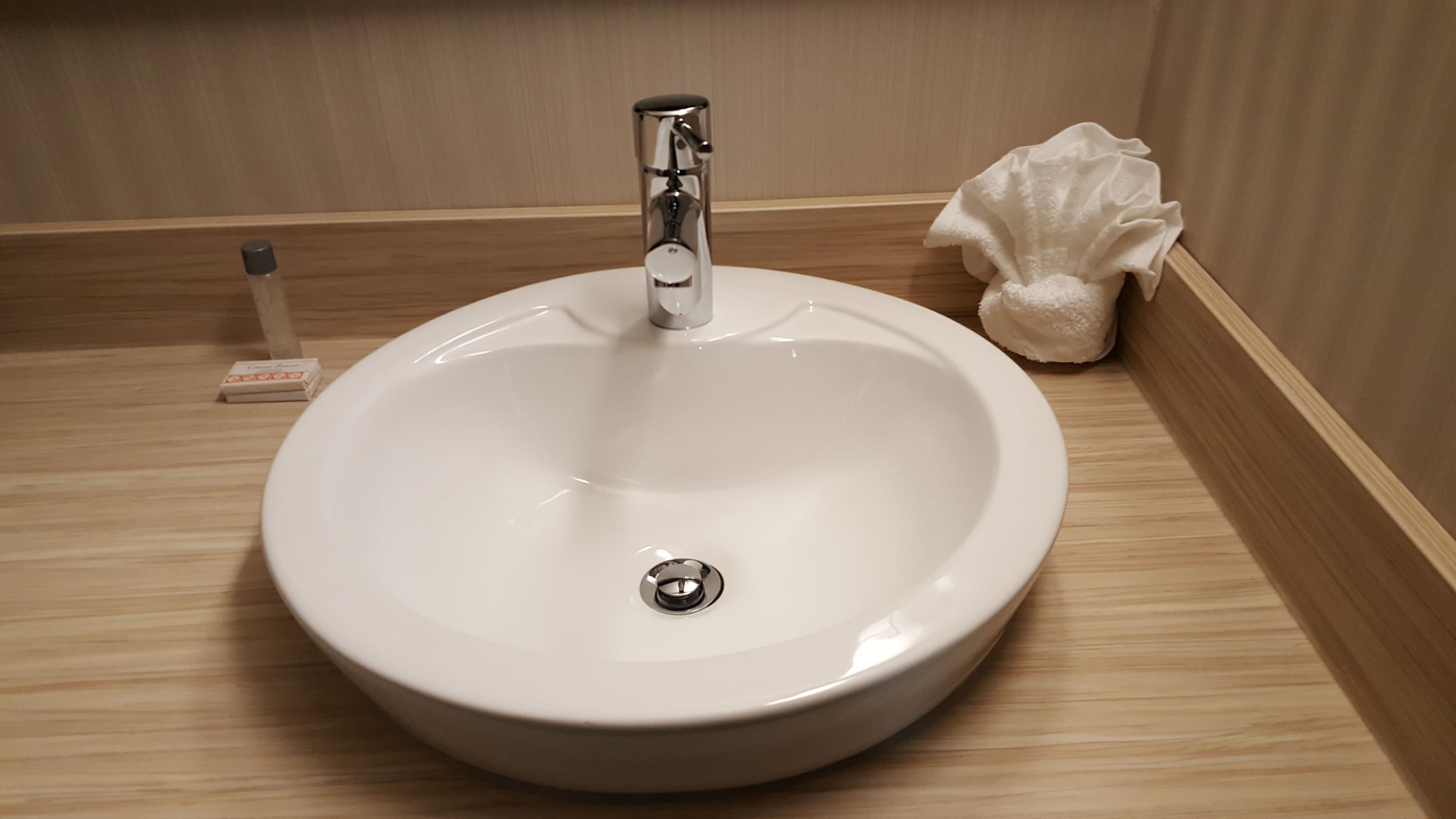 A white bathroom sink with a chrome faucet, a small tissue box, and a decorative shell on the wooden countertop.