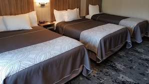 Una camera d'albergo con tre letti, ognuno con una coperta a fantasia, un comodino con una sveglia e una lampada a muro.