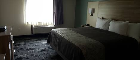 Ein Hotelzimmer mit einem großen Bett, einem Schreibtisch, einem Stuhl, einem Fenster mit Vorhängen, einer Klimaanlage und einem Nachttisch mit einer Lampe.