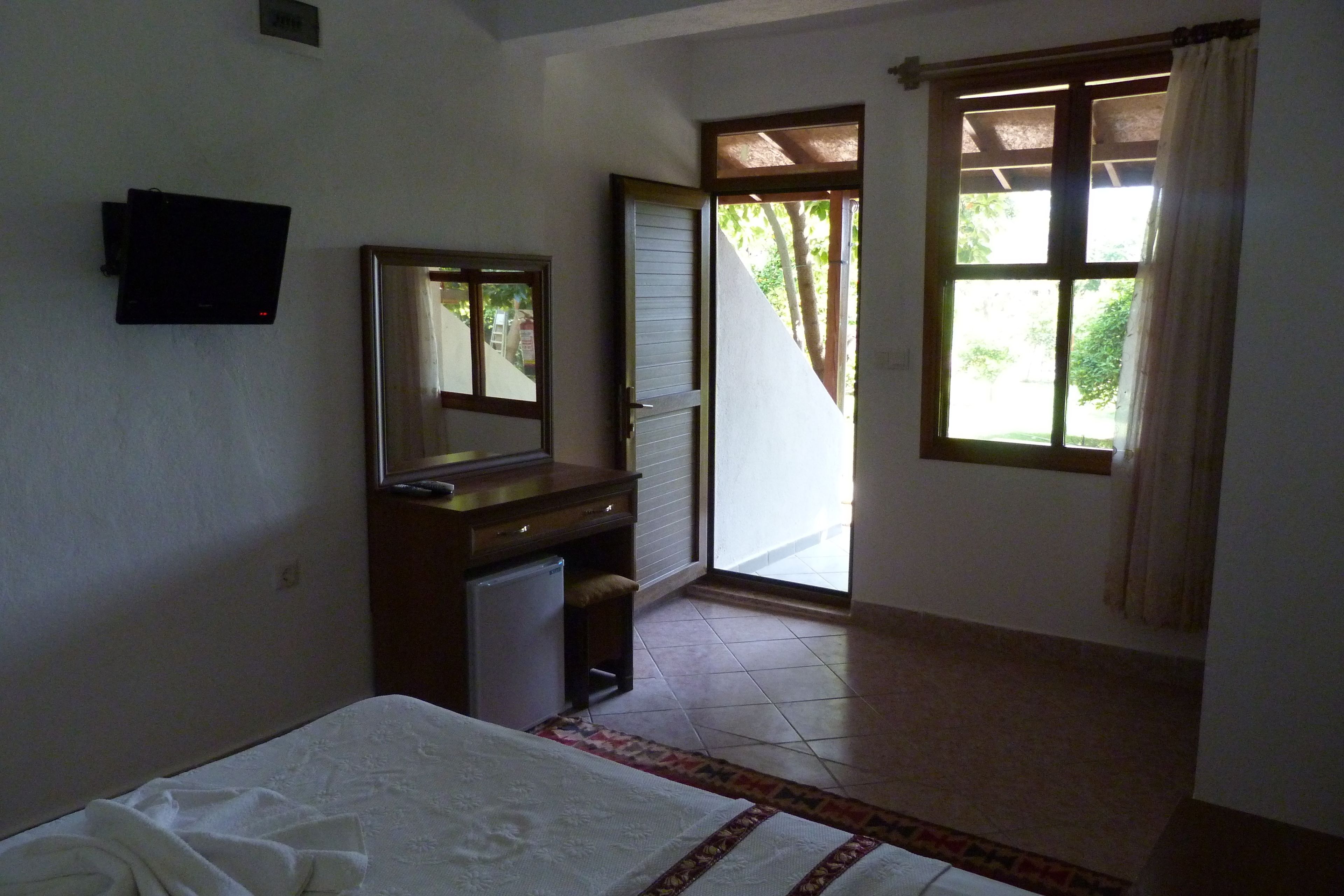A bedroom with a bed, a dresser, a television, and a door leading to a balcony.