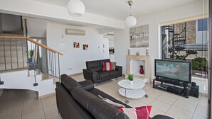 A modern living room with a sofa, coffee table, TV, and a staircase. - Esprit Villas (Neo Chorio)