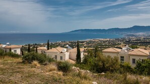 A coastal view with houses, a clear sky, and a distant mountain range. - Esprit Villas (Neo Chorio)