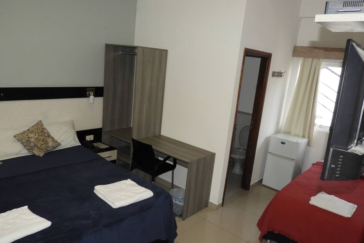 A hotel room with a bed, a desk, a chair, a TV, and a small kitchenette.
