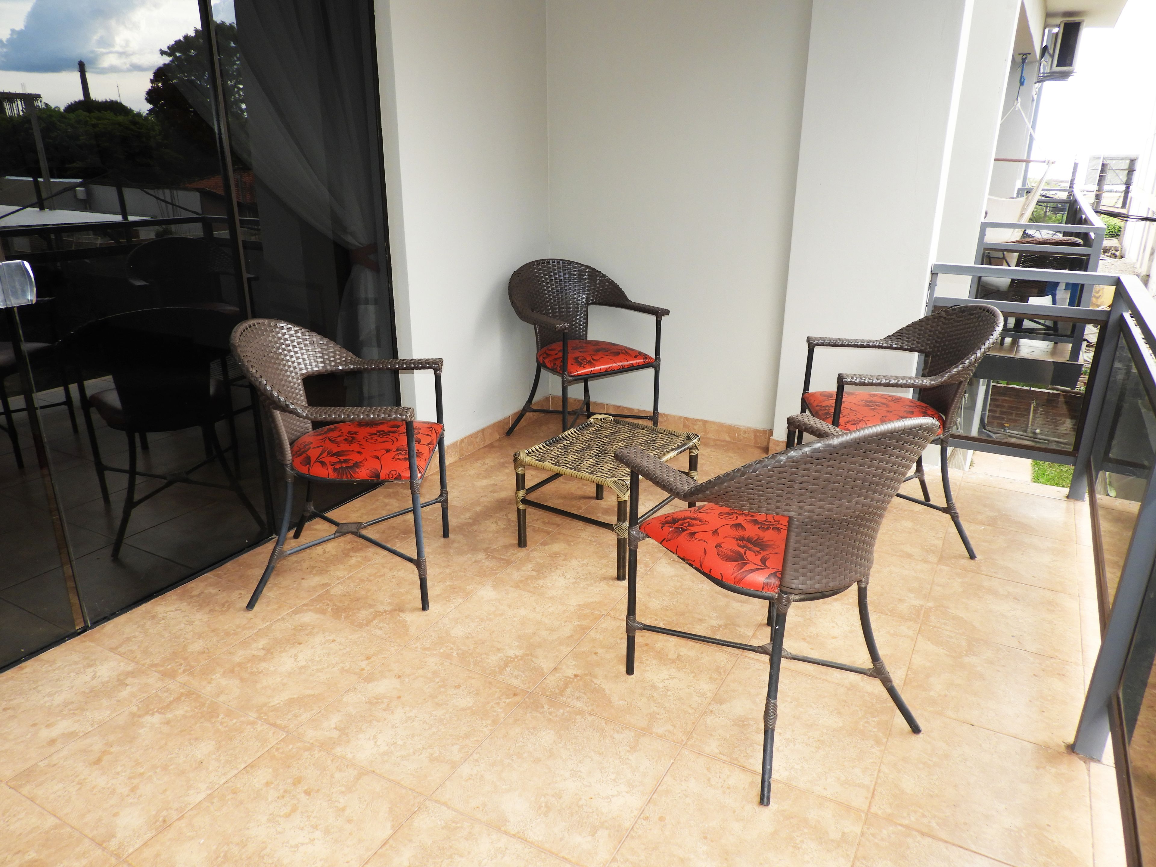 A balcony with four wicker chairs and a small table, featuring a tiled floor and a glass door leading to an outdoor area.