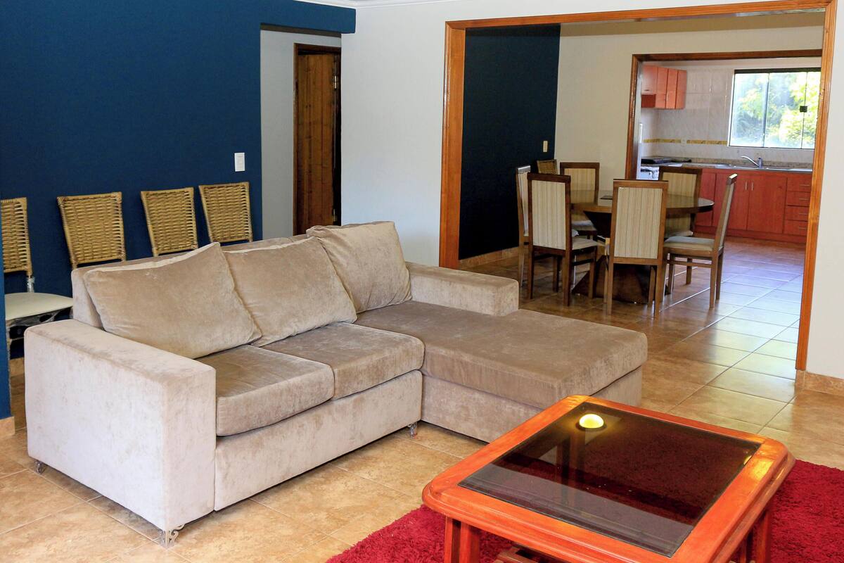 A living room with a beige sofa, a glass-top coffee table, and a red rug.