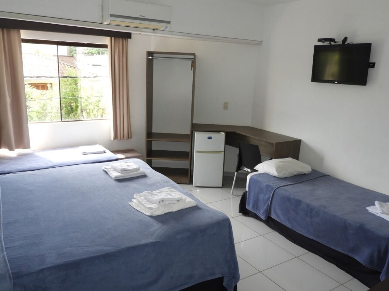 Habitación de hotel con dos camas, un escritorio, un televisor y un armario.