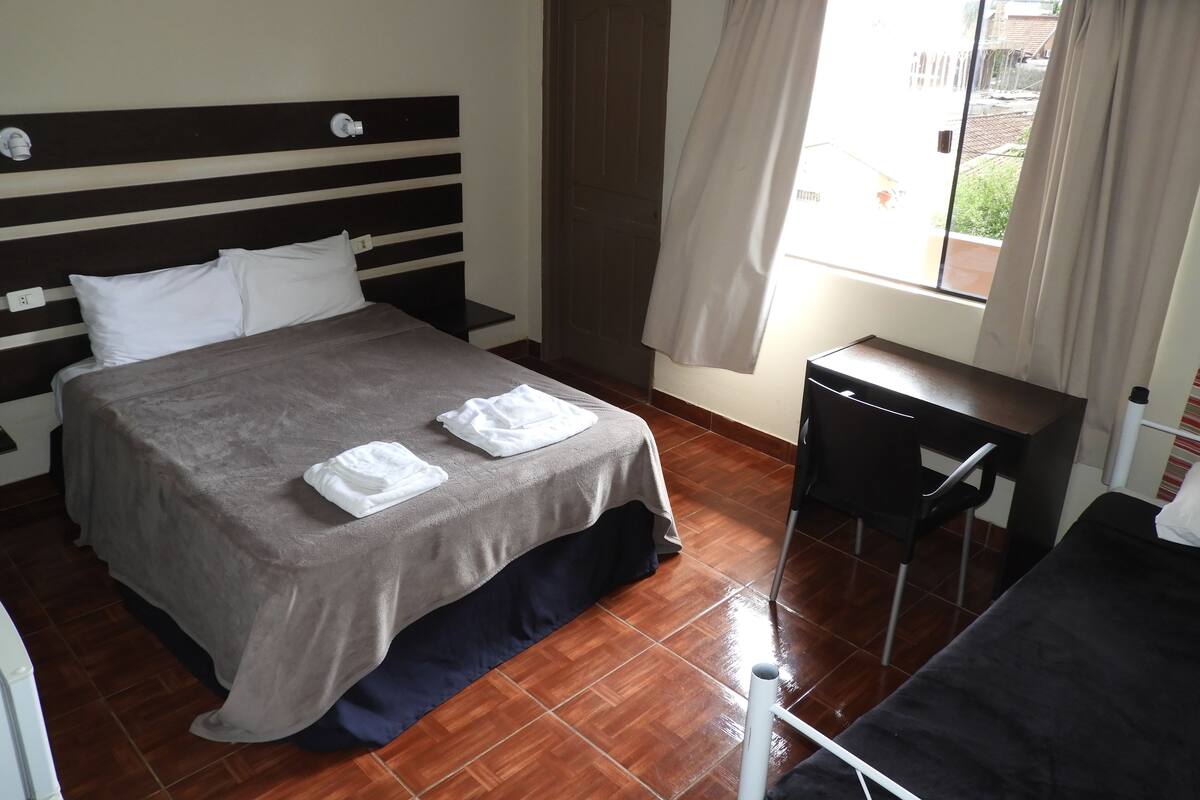 A hotel room with a bed, a desk, and a window.
