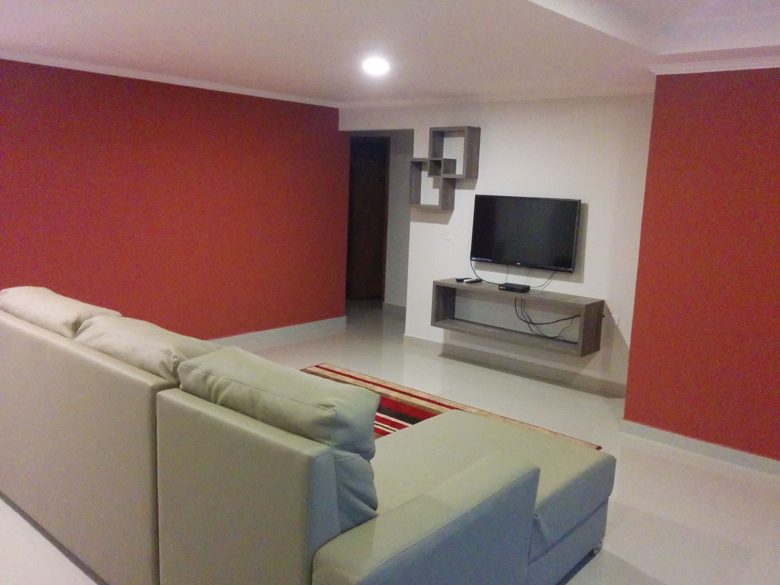 Een moderne woonkamer met een beige bank, een flatscreen televisie bevestigd aan een houten console, en rode muren.