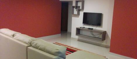 Een moderne woonkamer met een beige bank, een flatscreen televisie bevestigd aan een houten console, en rode muren.
