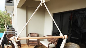 Uma cadeira rede suspensa no teto, cercada por mobiliário de vime e um chão de azulejos.