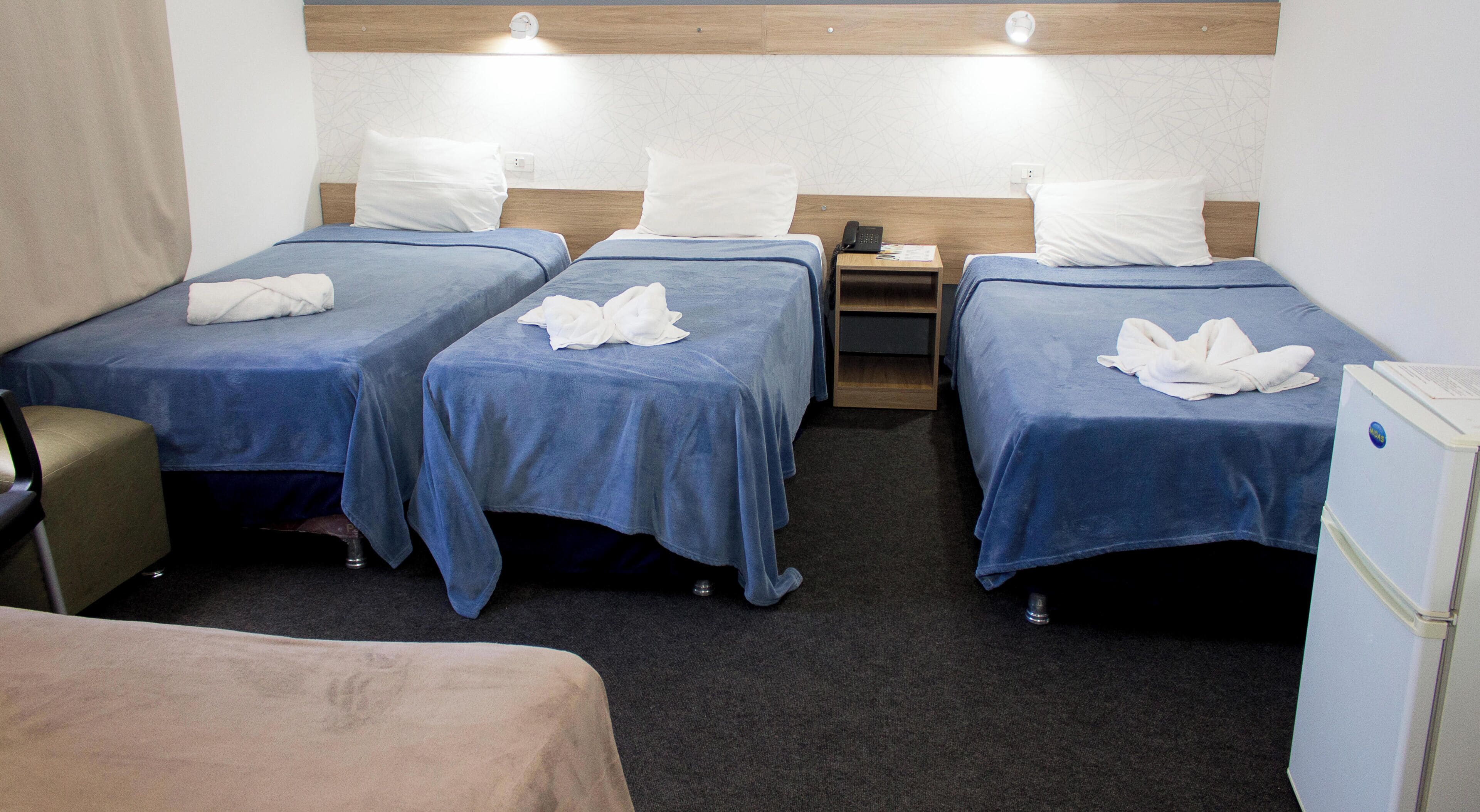 Habitación de hotel con cuatro camas individuales, un escritorio, una silla y un refrigerador.
