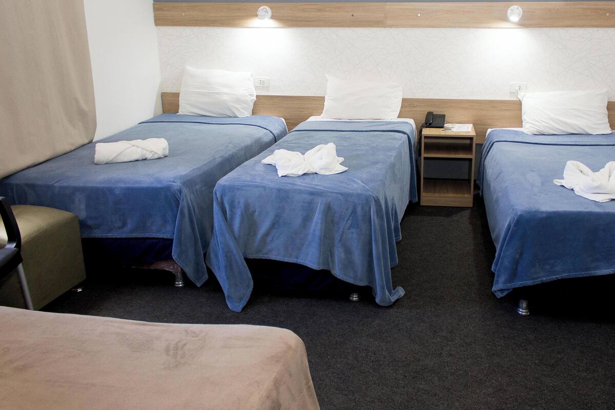 A hotel room with four single beds, a desk, a chair, and a refrigerator.