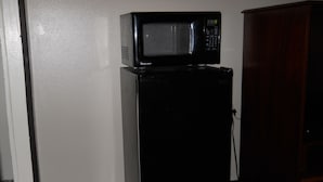 A black refrigerator with a microwave on top, a wooden cabinet to the right, and a white wall. - Value Inn Kenosha I-94 - Exit 344 (Kenosha)