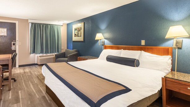 A hotel room with a large bed, two bedside lamps, a desk with a chair, and a window with curtains. - Value Inn Kenosha I-94 - Exit 344 (Kenosha)