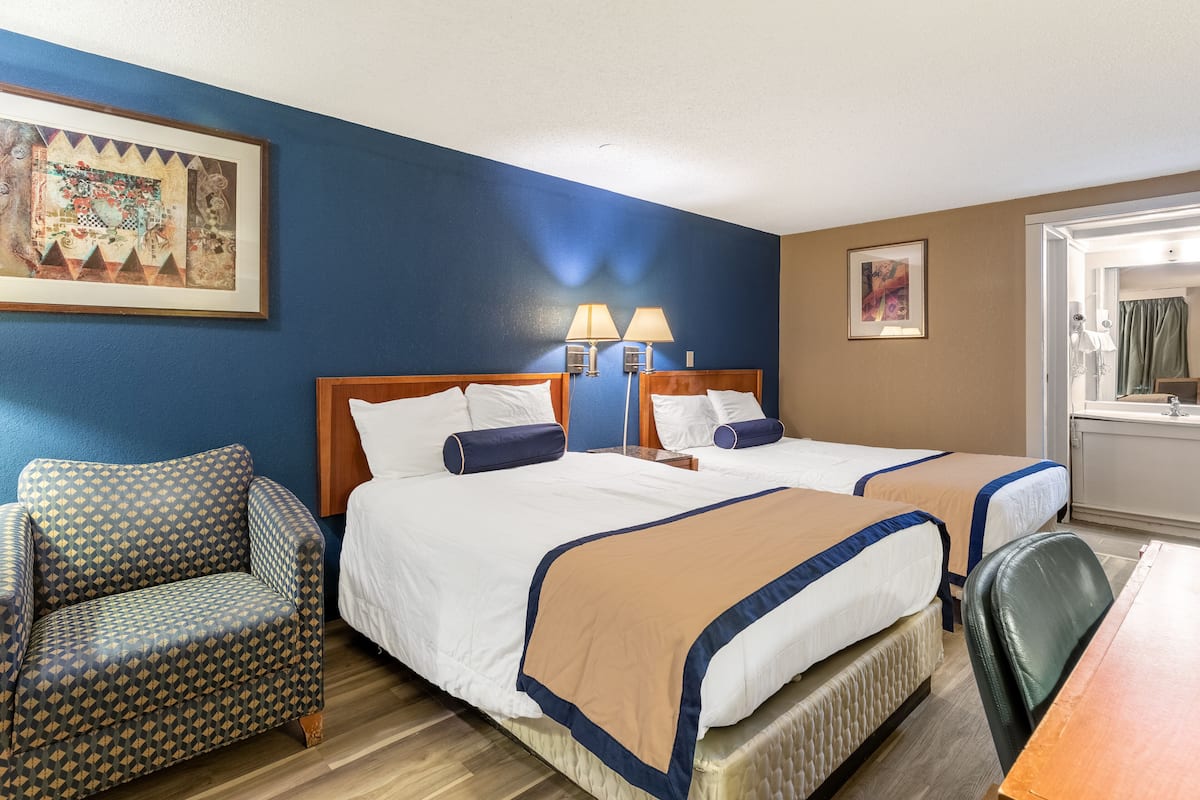 Ein Hotelzimmer mit zwei Betten, einem Sofa, einem Schreibtisch und einem durchgehenden Türspalt einsehbarer Badezimmer.