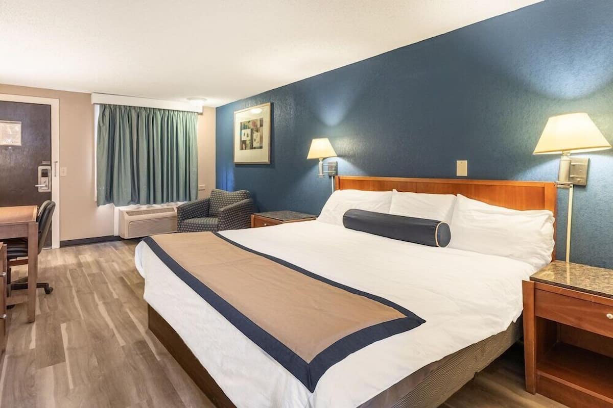 Ein Hotelzimmer mit einem großen Bett, zwei Nachttischlampen, einem Schreibtisch mit Stuhl und einem Fenster mit Vorhängen.