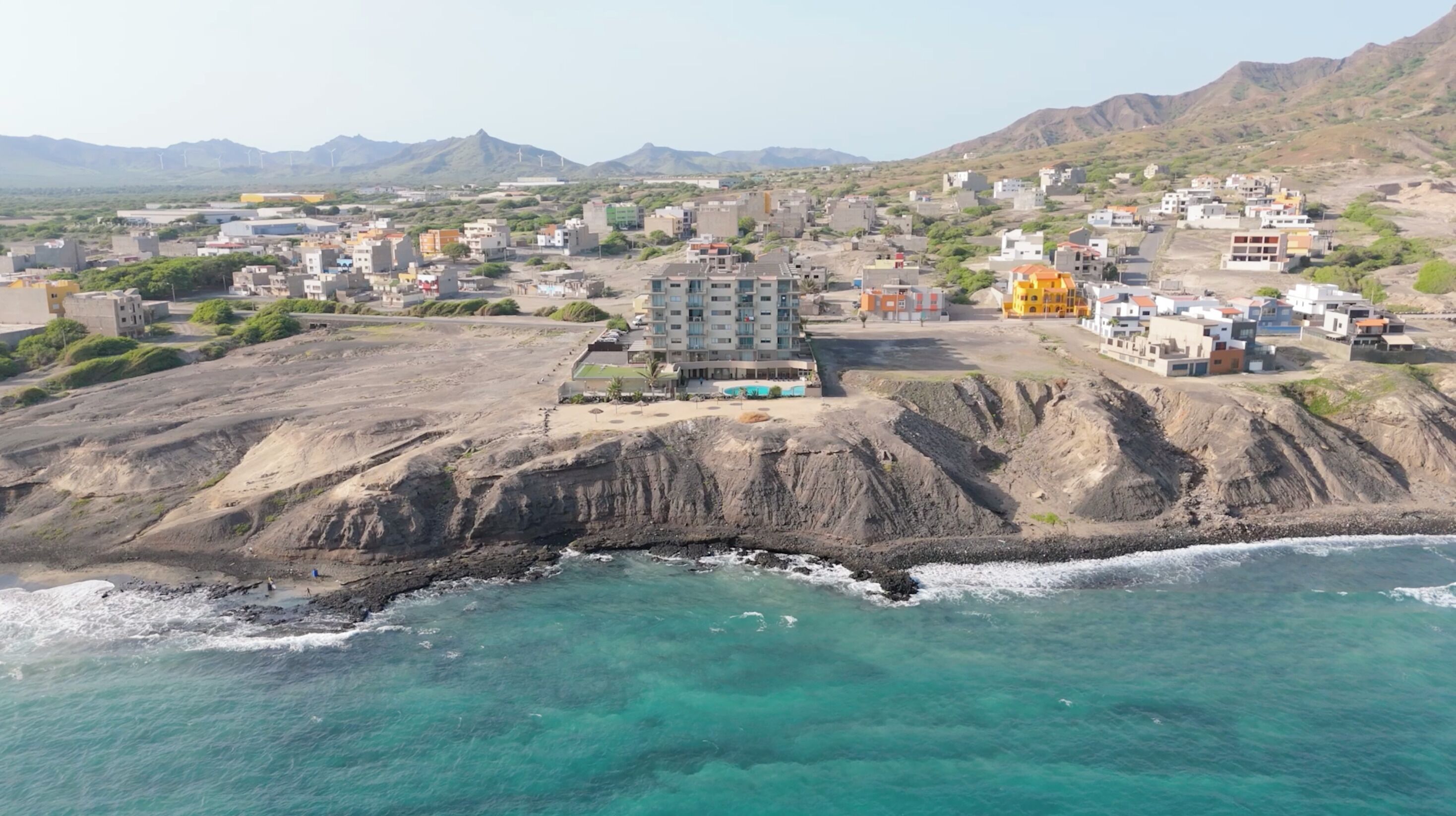 Un pueblo costero con un hotel destacado que cuenta con un patio central, situado en un acantilado con vistas al mar.